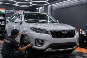 A silver SUV parked in a modern Indian detailing studio with a technician mid-way through applying clear paint protection film to the front bumper, Indian flag colors subtly visible on branding signage in the background, professional lighting, photorealistic