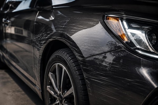 Car with visible scratches and scuff marks on the side panel.