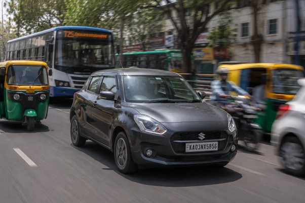 A compact hatchback navigating through busy Bangalore traffic with auto-rickshaws and buses around it, motion blur on the background, midday lighting, photorealistic street photography.