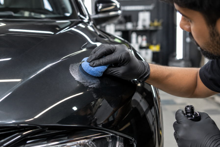 Detailer applying a small amount of polish with a cloth to a car's paint surface for testing, focused hands-on technique, workshop lighting, professional automotive service photography style
