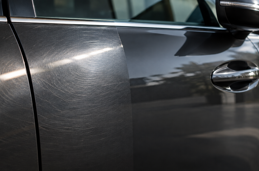 Close-up of a car door panel showing faint swirl marks catching light on one side, smooth glossy finish on the other, soft directional lighting, automotive detail photography style